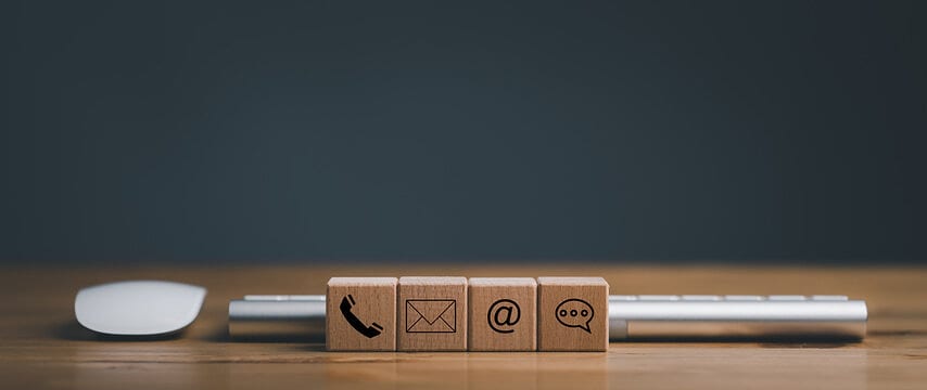 Wooden blocks showing phone, envelope, at-sign, and chat-bubble icons, the everyday ways to get in touch.